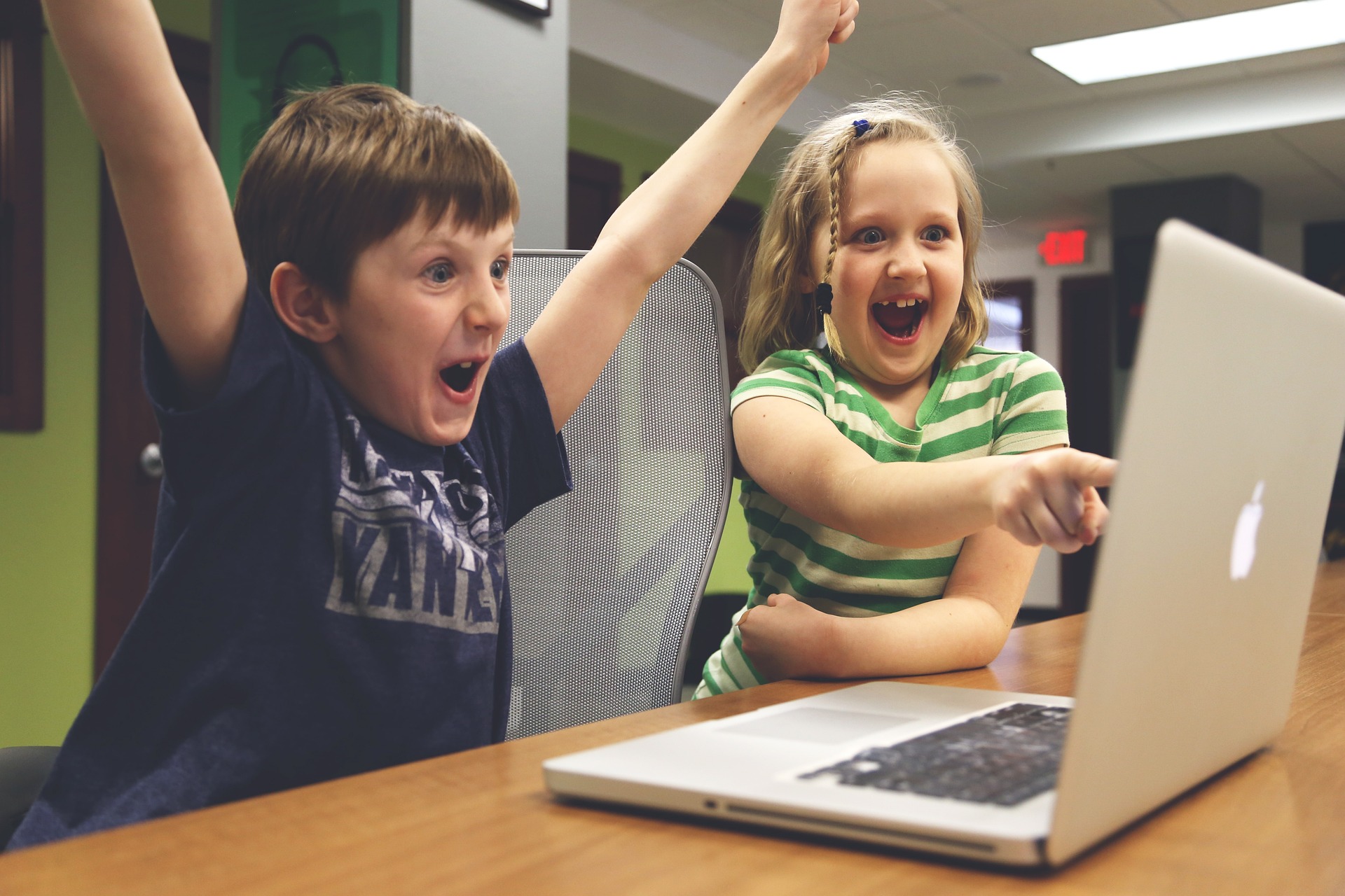 Two kids cheering infront of a laptop