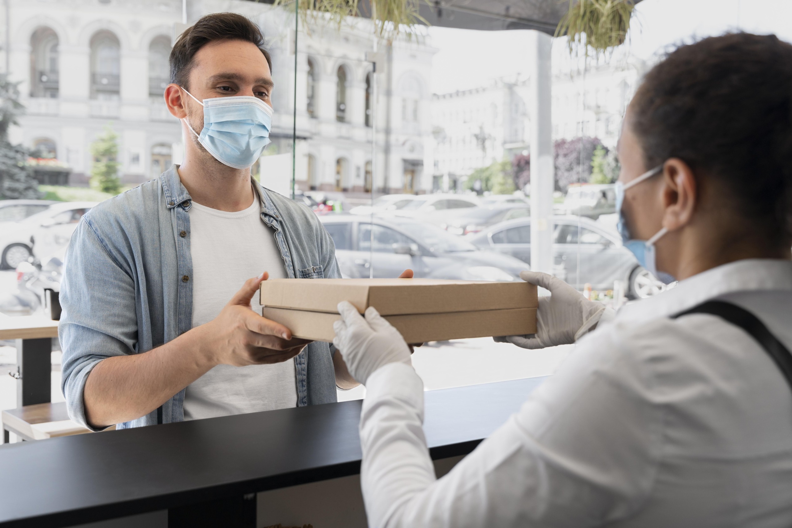 woman-with-apron-offering-packed-takeaway-food-male-customer